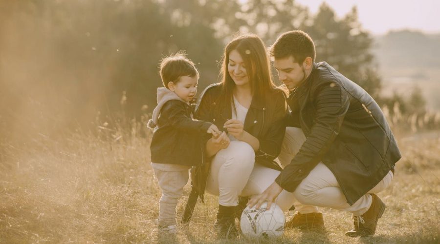 A cheerful family bonding outdoors with a soccer ball, enjoying a sunny day in the grass.